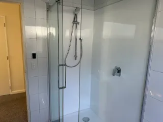 Walk-in shower with white tiles, glass door and chrome fixtures